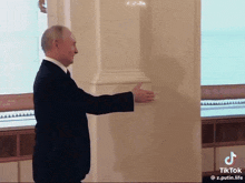 a man in a suit and tie is standing in front of a white wall with a tiktok watermark
