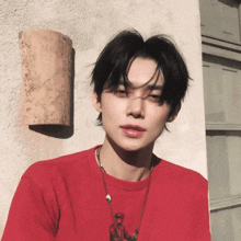 a young man wearing a red t-shirt is standing in front of a wall