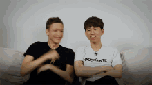 a man wearing a descente shirt sits next to another man on a couch