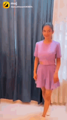 a girl in a purple top and skirt is standing in front of a window .