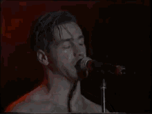 a man without a shirt singing into a microphone in a dark room