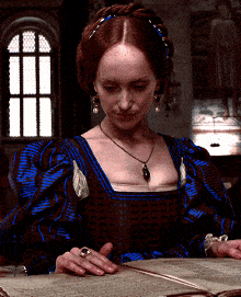 a woman in a blue and brown dress is sitting at a table reading a book