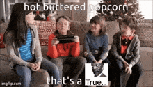 a group of children are sitting on a couch playing a video game while eating hot buttered popcorn .