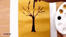 a person is painting a tree on a yellow background with drawbook written below it