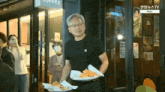 a man in a black shirt is carrying a tray of food in front of a coffee shop