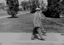 a black and white photo of two men walking down a sidewalk in a park
