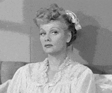 a black and white photo of a woman sitting on a bed wearing a robe .