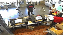 a man and a child are standing at a counter in a restaurant with a camera that says camera 17 on it .