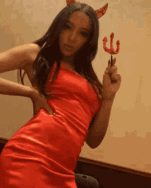 a woman in a red dress with horns is holding a red trident