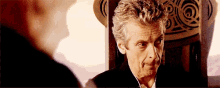 a man in a suit and tie is sitting in a chair and looking at another man .
