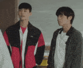 two young men are standing next to each other in a room and talking to each other .
