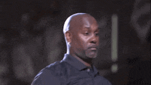 a bald man in a black shirt looks at the camera