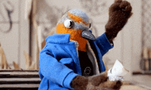 a stuffed bird wearing a blue jacket holds a piece of paper in its hand