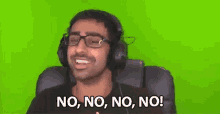 a man wearing headphones and glasses is sitting in front of a green screen and saying no .
