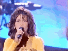 a woman singing into a microphone while wearing a yellow top