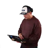 a man wearing headphones and a hat holds a laptop with facebook stickers on it
