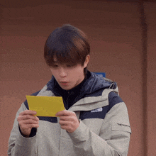 a man wearing a north face jacket holds a yellow piece of paper in his hands
