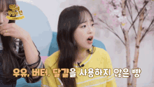 a girl in a yellow sweater is talking into a microphone with korean writing on the bottom