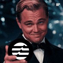 a man in a tuxedo is smiling and holding a black circle with a white circle with the letter m on it
