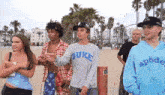 a group of people standing on a beach one of them wearing a duke shirt