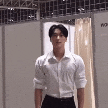 a man in a white shirt and black pants is standing in front of a dressing room .
