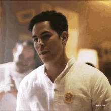 a man wearing a white shirt has a gold smiley face pin on his chest