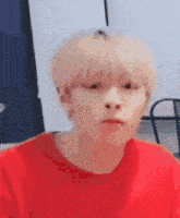 a young man with blonde hair is wearing a red shirt .