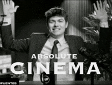 a man in a suit and tie is standing in front of a microphone with his arms in the air and the words absolute cinema above him