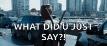 a man in a deadpool costume is standing in a parking lot holding a gun and asking what did u just say .