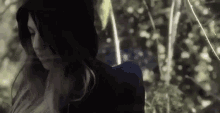 the woman is wearing a hooded jacket and standing in the woods .
