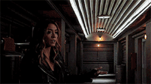 a woman in a black jacket is standing in a dark hallway with a striped ceiling .