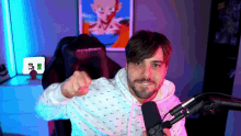 a man in a white hoodie holds a microphone and points at the camera