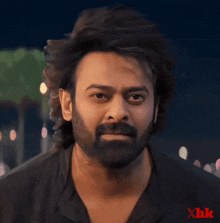 a man with a beard is looking at the camera with a xhk logo in the corner