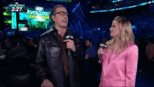 a woman in a pink suit is talking to a man in a leather jacket with a microphone in front of an aew sign