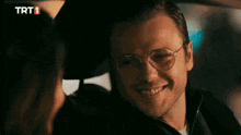 a man wearing glasses is looking at a woman in a car with trt1 written on the screen
