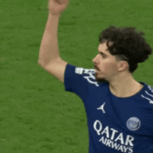 a man wearing a blue qatar airways shirt waves his hand