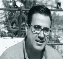 a black and white photo of a man wearing glasses and a jacket .