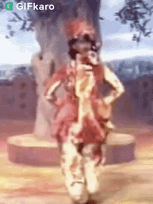 a person is dancing in front of a tree with a gifkaro logo in the corner