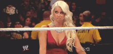 a woman in a red dress stands in a wrestling ring with a security guard in the background