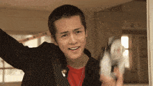 a young man in a red shirt and black jacket is smiling and holding a camera