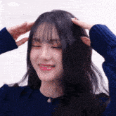 a woman wearing a blue sweater has her eyes closed and her hands on her head