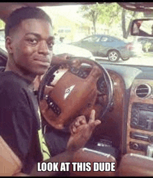 a man is sitting in a car with a bentley steering wheel and giving the middle finger .