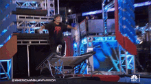 a man in an american ninja warrior t-shirt jumps over a trampoline