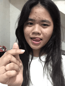 a girl with long black hair is sticking her tongue out and making a heart sign