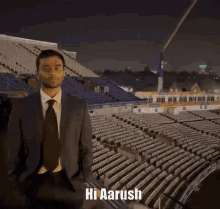 a man in a suit and tie says hi aarush in front of a stadium