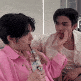 a man in a pink jacket is drinking water through a straw while another man in a white shirt looks on .
