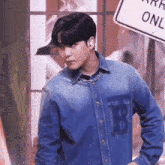 a young man wearing a denim shirt and a necklace is standing in front of a sign .