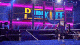 a man in a blue shirt with the word us me on it walks out of a wrestling ring