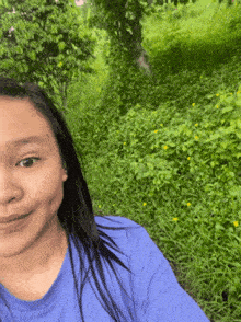 a woman in a blue shirt is taking a selfie in front of a lush green field .
