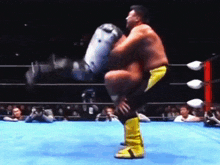 a wrestler in a yellow and black outfit is standing on a blue mat in a wrestling ring